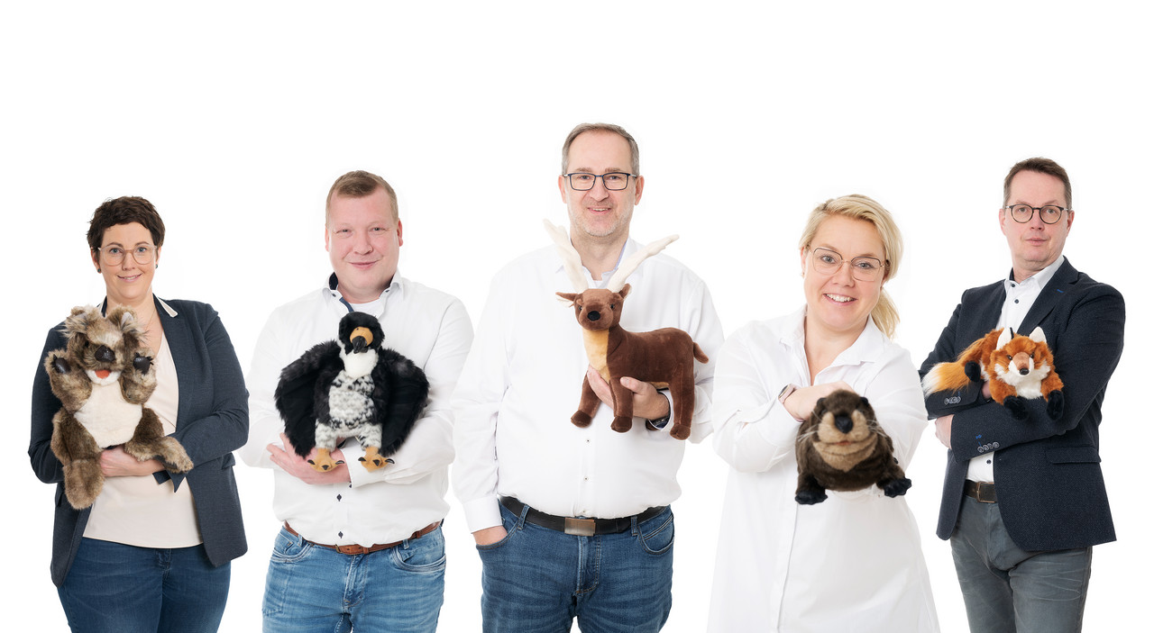 Gruppe von fünf lächelnden Personen vor weißem Hintergrund.